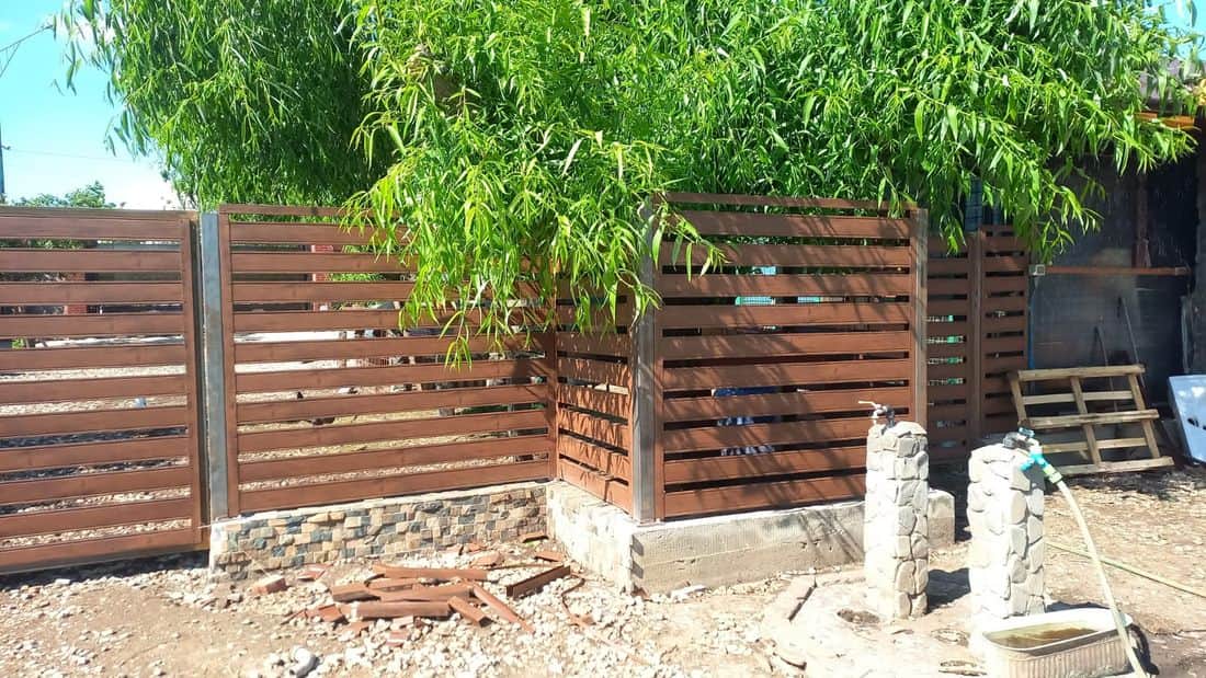 Gard metalic cu șipcă orizontală, finisaj lemn, montat pe soclu de piatră