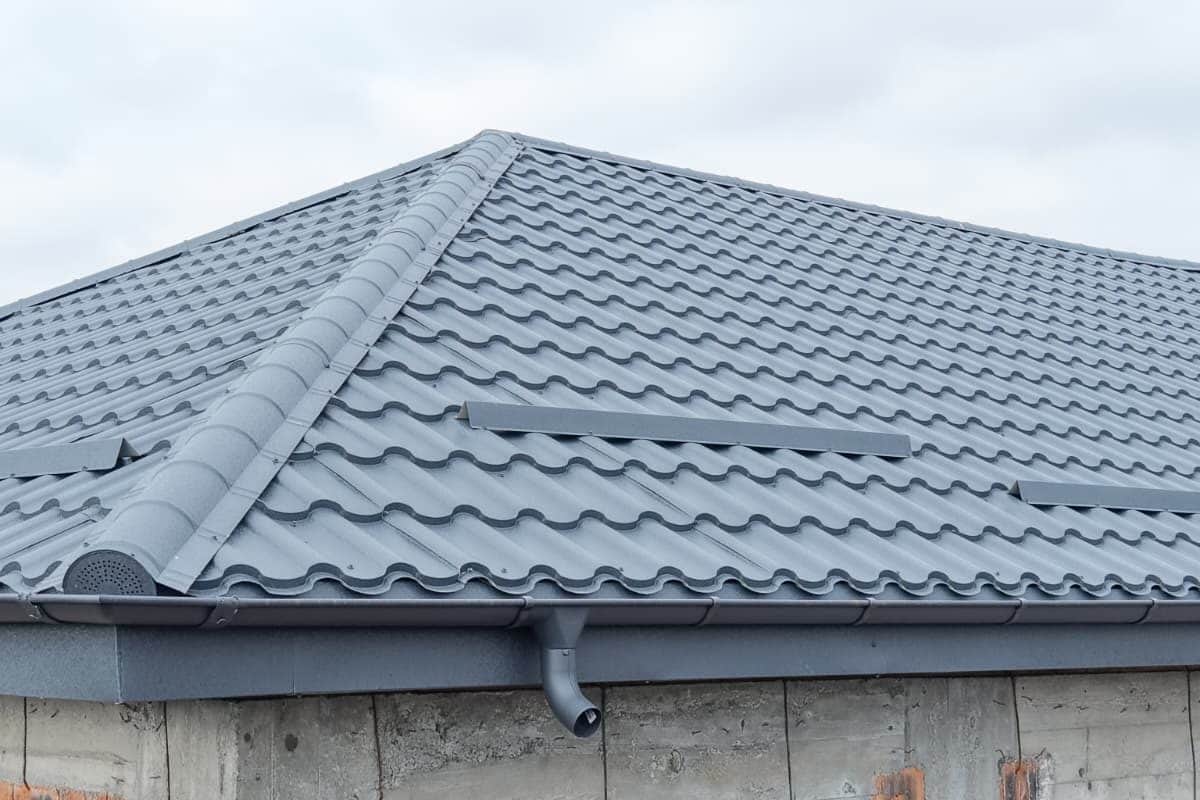 Acoperiș în patru ape din țiglă metalică gri, finalizat pe o casă la roșu