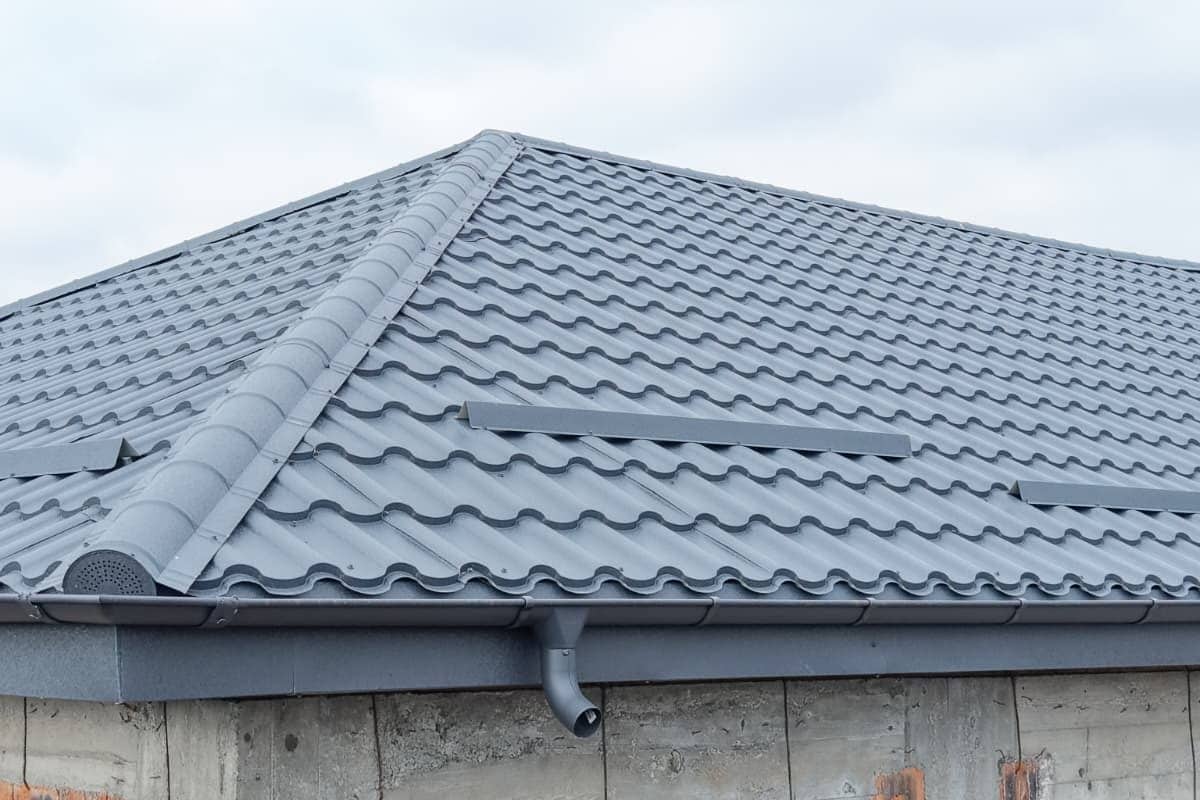 Acoperiș în patru ape din țiglă metalică gri, finalizat pe o casă la roșu